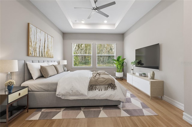 bedroom with ceiling fan, light wood-type flooring, and a tray ceiling