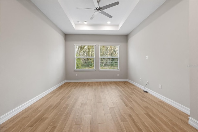 empty room featuring a raised ceiling, ceiling fan, and light wood-type flooring