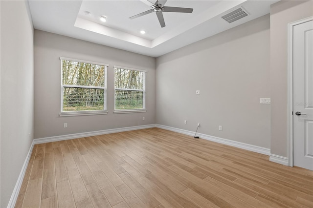 spare room featuring light wood-type flooring, a tray ceiling, and ceiling fan