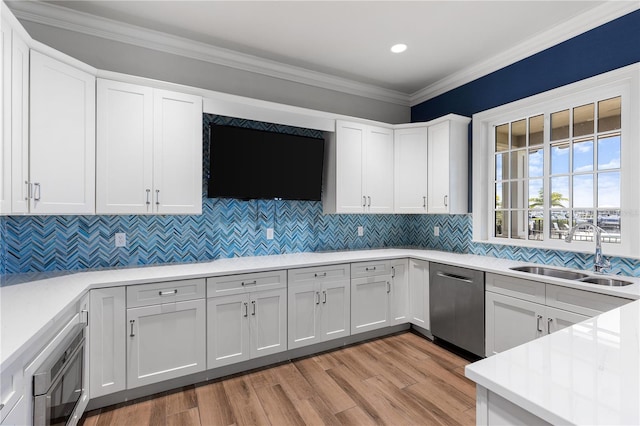 kitchen with ornamental molding, stainless steel appliances, sink, white cabinets, and light hardwood / wood-style floors