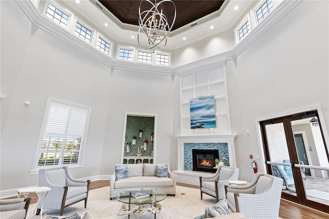 living room with french doors, a towering ceiling, ornamental molding, wood-type flooring, and a chandelier