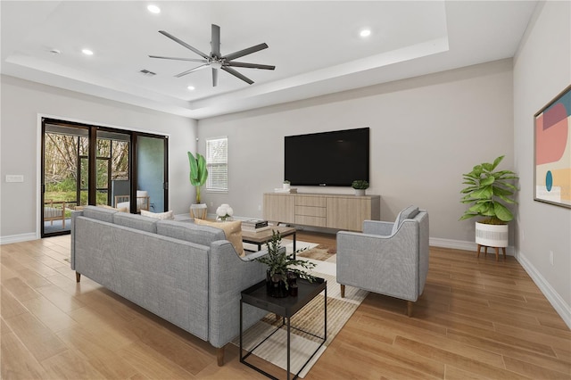 living room with a tray ceiling, light hardwood / wood-style flooring, and ceiling fan