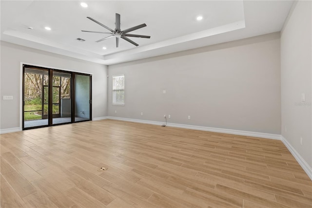 unfurnished room featuring ceiling fan, light wood-type flooring, and a tray ceiling