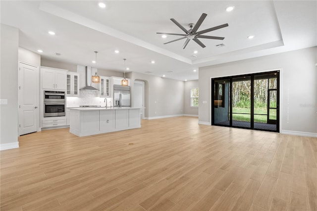 unfurnished living room featuring ceiling fan, a raised ceiling, sink, and light hardwood / wood-style flooring