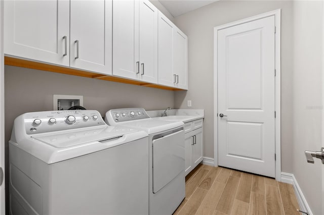 clothes washing area featuring cabinets, independent washer and dryer, sink, and light hardwood / wood-style flooring