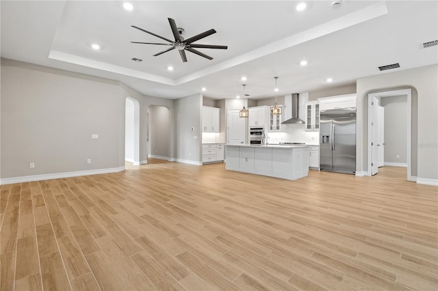 unfurnished living room featuring ceiling fan, a raised ceiling, sink, and light hardwood / wood-style flooring