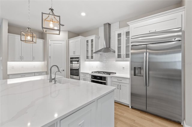 kitchen featuring appliances with stainless steel finishes, wall chimney exhaust hood, pendant lighting, white cabinets, and light hardwood / wood-style floors