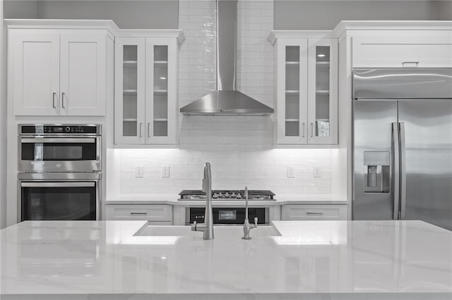 kitchen with light stone countertops, stainless steel appliances, white cabinets, and wall chimney range hood