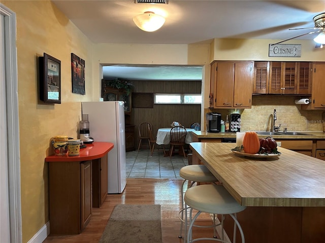 kitchen with white refrigerator, decorative backsplash, sink, ceiling fan, and light hardwood / wood-style flooring