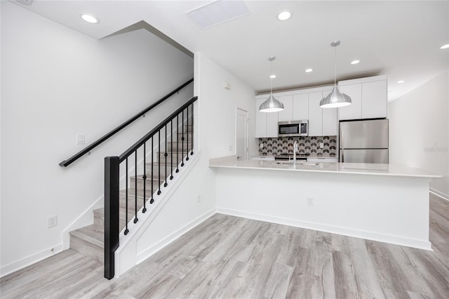 kitchen with kitchen peninsula, decorative light fixtures, light hardwood / wood-style floors, white cabinetry, and stainless steel appliances