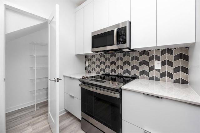 kitchen with light hardwood / wood-style floors, white cabinetry, backsplash, and appliances with stainless steel finishes