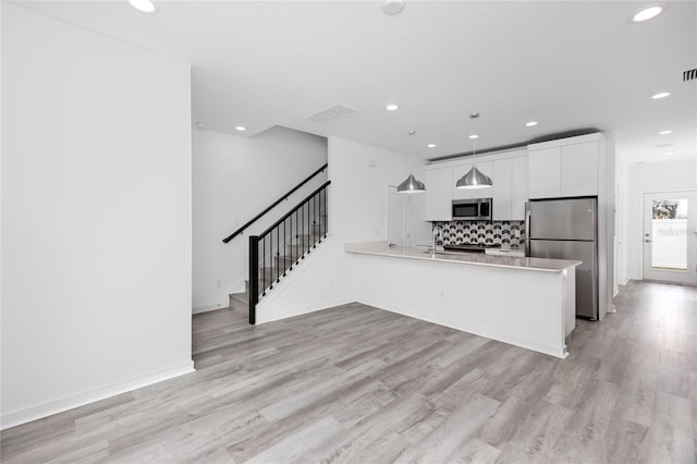 kitchen with kitchen peninsula, white cabinetry, stainless steel appliances, and light hardwood / wood-style flooring