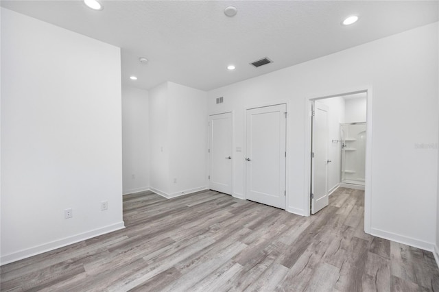 unfurnished bedroom with a textured ceiling, light hardwood / wood-style flooring, and ensuite bath