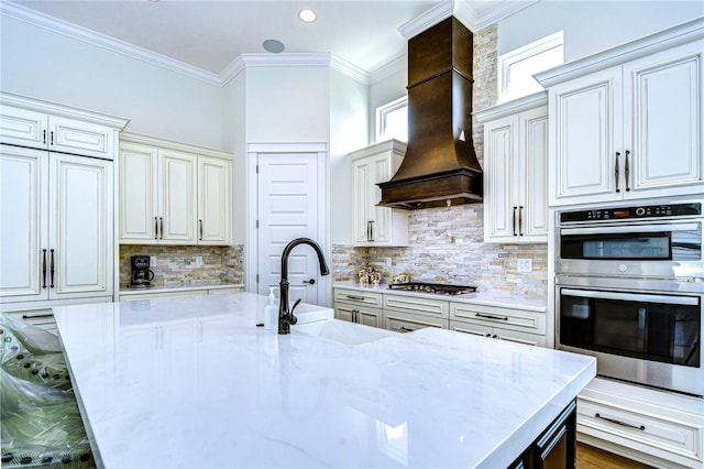 kitchen with sink, stainless steel appliances, light stone counters, premium range hood, and decorative backsplash