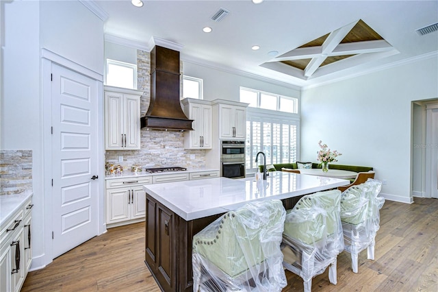 kitchen with a breakfast bar, light wood-type flooring, custom range hood, and an island with sink