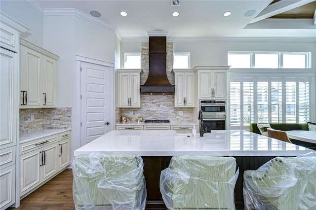 kitchen featuring a kitchen breakfast bar, decorative backsplash, a large island, and custom range hood