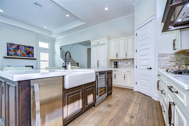 kitchen featuring beverage cooler, tasteful backsplash, light hardwood / wood-style flooring, extractor fan, and white cabinets