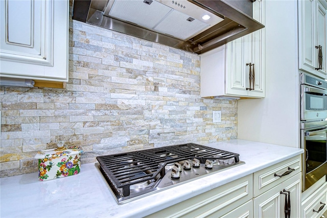 kitchen featuring white cabinets, decorative backsplash, wall chimney range hood, and appliances with stainless steel finishes