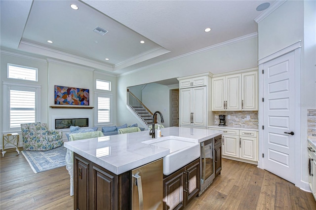 kitchen featuring decorative backsplash, dark brown cabinets, a kitchen island with sink, sink, and hardwood / wood-style floors