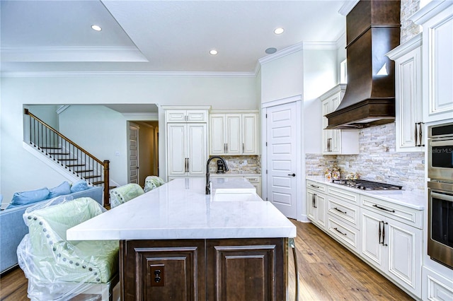 kitchen with sink, stainless steel gas cooktop, a kitchen island with sink, a breakfast bar, and custom range hood