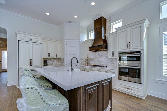 kitchen featuring appliances with stainless steel finishes, ornamental molding, light hardwood / wood-style flooring, a breakfast bar area, and an island with sink