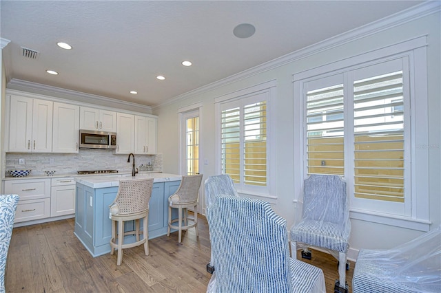 kitchen with white cabinetry, light hardwood / wood-style flooring, an island with sink, a breakfast bar, and appliances with stainless steel finishes