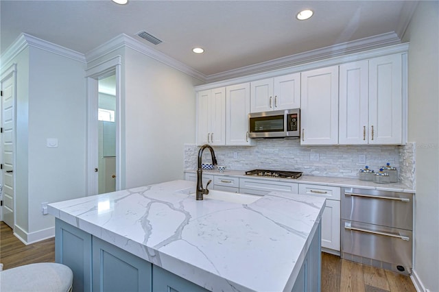 kitchen with light stone countertops, appliances with stainless steel finishes, dark hardwood / wood-style flooring, white cabinetry, and an island with sink