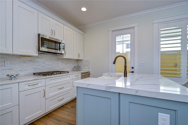 kitchen featuring white cabinetry, sink, stainless steel appliances, crown molding, and a center island with sink