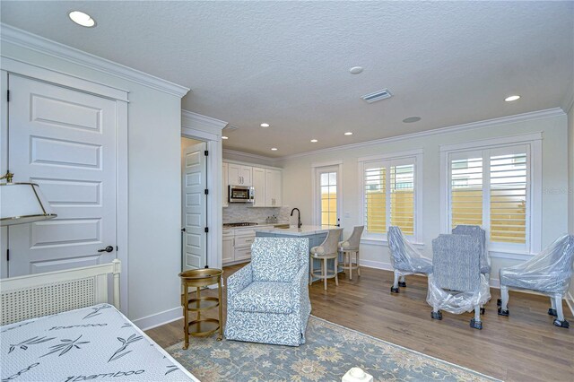 interior space with a textured ceiling, sink, crown molding, and light hardwood / wood-style flooring