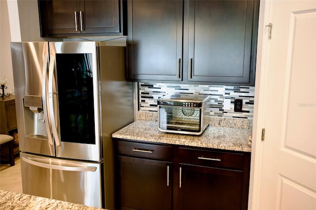 kitchen featuring decorative backsplash, light stone counters, stainless steel fridge with ice dispenser, and dark brown cabinetry