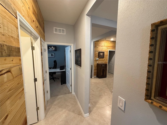 corridor with light tile patterned flooring and wooden walls