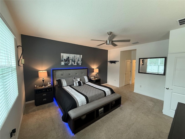 carpeted bedroom with a textured ceiling, multiple windows, and ceiling fan