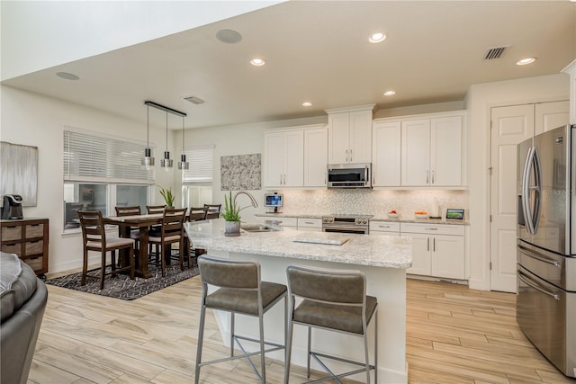 kitchen featuring sink, appliances with stainless steel finishes, a kitchen island with sink, white cabinets, and decorative light fixtures