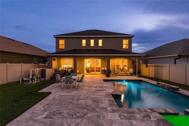 back house at dusk with a patio, a fenced in pool, and pool water feature