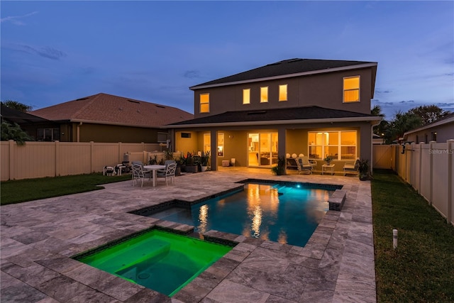 back house at dusk featuring a pool with hot tub and a patio area