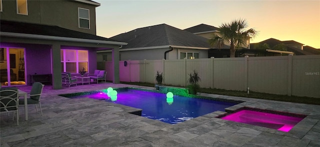 pool at dusk featuring a patio and an in ground hot tub