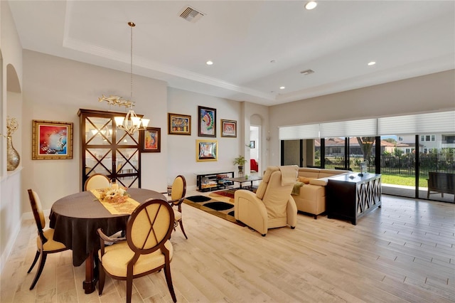 living room with light wood-type flooring, a notable chandelier, and a raised ceiling