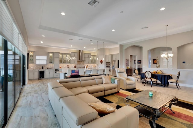 living room with light wood-type flooring, a chandelier, and beverage cooler