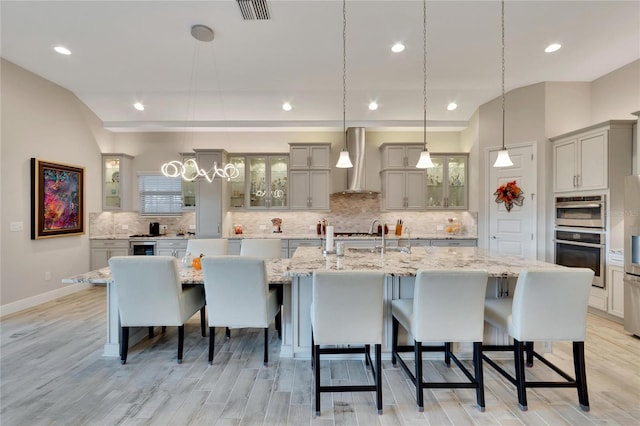 kitchen featuring light hardwood / wood-style floors, wall chimney range hood, a spacious island, and decorative light fixtures