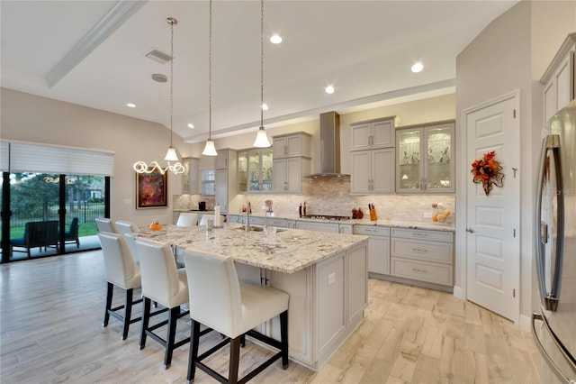 kitchen featuring stainless steel appliances, a kitchen island with sink, gray cabinets, wall chimney range hood, and light hardwood / wood-style flooring