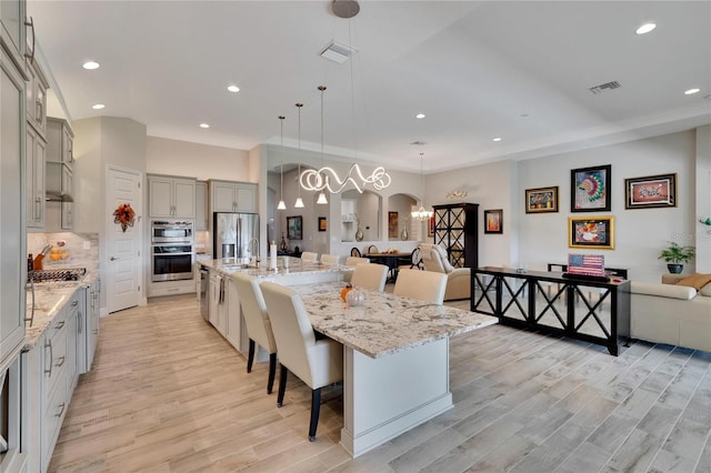 kitchen featuring light hardwood / wood-style floors, stainless steel appliances, hanging light fixtures, a breakfast bar area, and a large island with sink