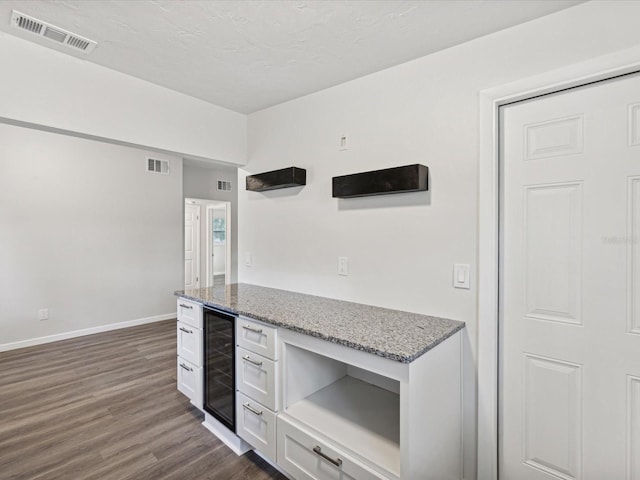 kitchen featuring dark wood-type flooring, light stone countertops, beverage cooler, and white cabinetry