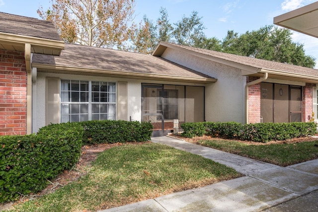 doorway to property featuring a shingled roof, brick siding, a yard, and stucco siding