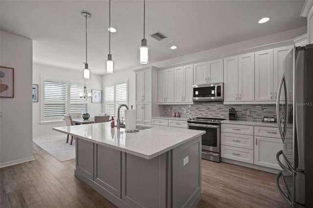 kitchen with a center island with sink, white cabinetry, appliances with stainless steel finishes, decorative light fixtures, and dark wood-type flooring