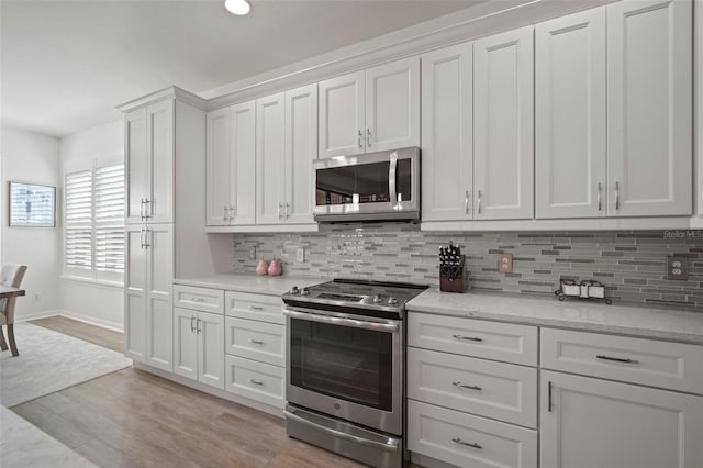 kitchen with light stone counters, white cabinetry, appliances with stainless steel finishes, backsplash, and light hardwood / wood-style flooring