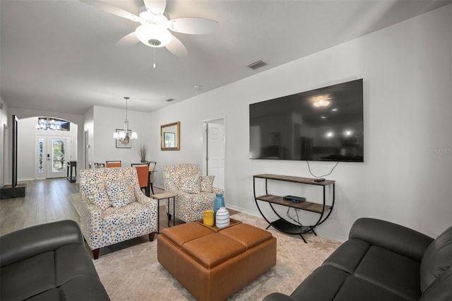 living room featuring french doors, ceiling fan with notable chandelier, and light hardwood / wood-style flooring