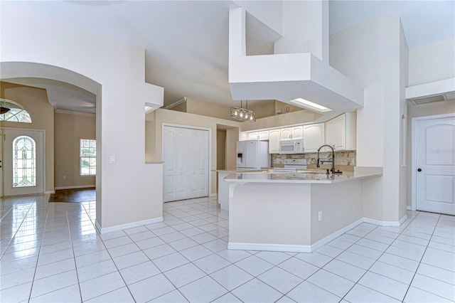 kitchen with kitchen peninsula, white appliances, light tile patterned flooring, and white cabinets