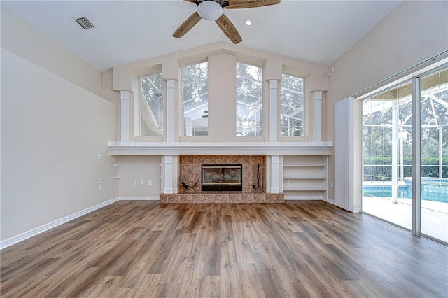 unfurnished living room featuring ceiling fan, hardwood / wood-style flooring, a tiled fireplace, and vaulted ceiling