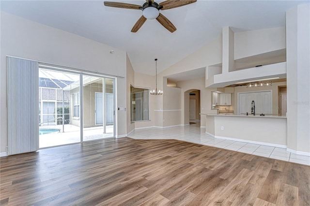 unfurnished living room with high vaulted ceiling, light wood-type flooring, and ceiling fan with notable chandelier