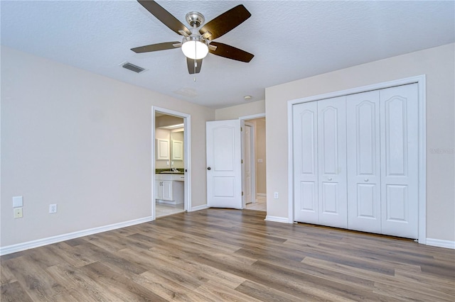 unfurnished bedroom with a closet, ensuite bath, a textured ceiling, hardwood / wood-style flooring, and ceiling fan